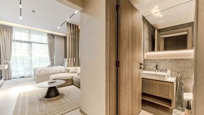 Una habitación de hotel moderna con sofá, una mesita de centro, un armario de madera y un baño con lavabo y espejo.