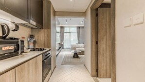 Una cocina moderna con microondas, estufa y armarios. Un pasillo conduce a una sala de estar con sofá y una mesa de centro.