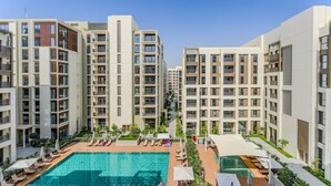 A modern apartment complex with a central swimming pool, multiple balconies, and a clear sky. - HAVN - 1 Bed in Cedar 3, Creek Harbour (Dubai)