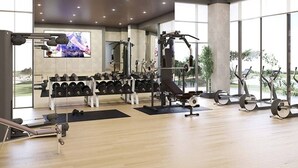 A modern gym with weightlifting equipment, cardio machines, and a TV screen. - HAVN - 1 Bed in Cedar 3, Creek Harbour (Dubai)