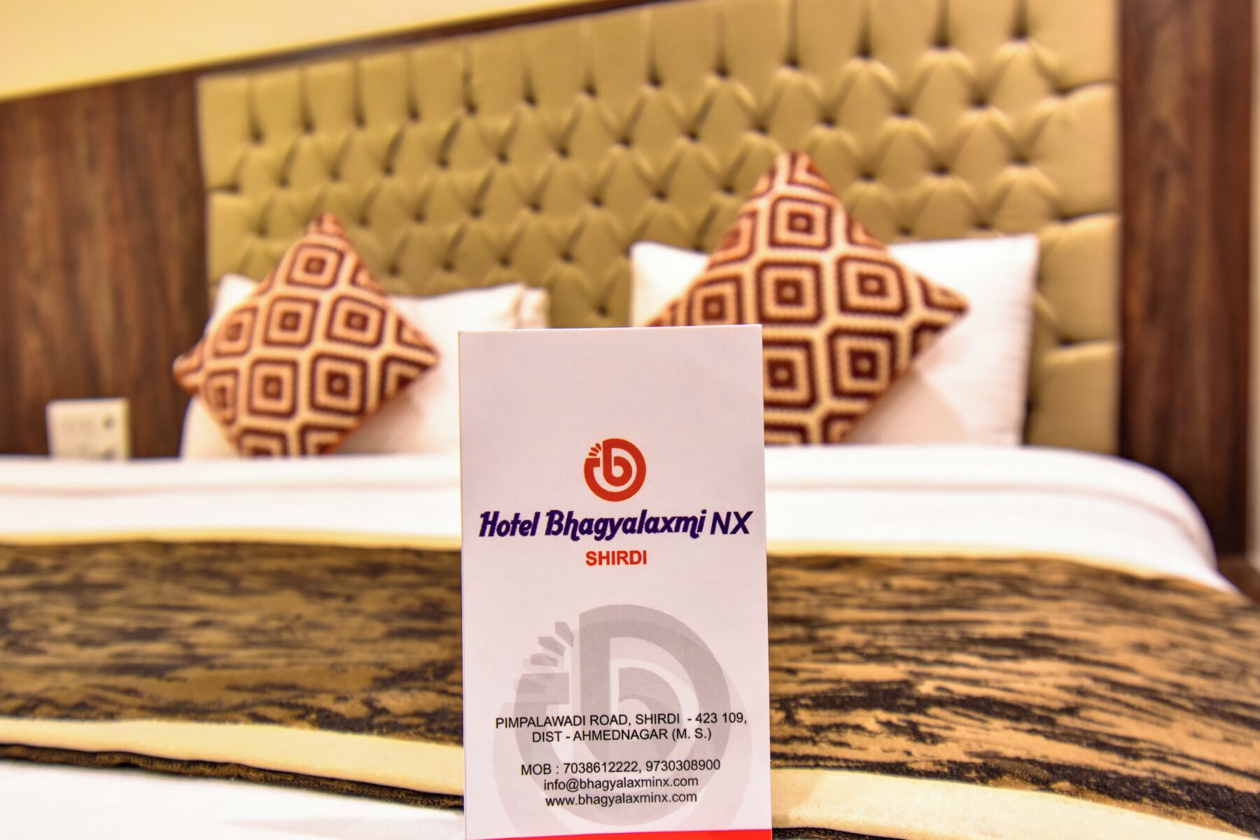 Une enseigne d’hôtel portant le nom « Hotel Bhagyalaxmi NX » et indiquant les coordonnées.