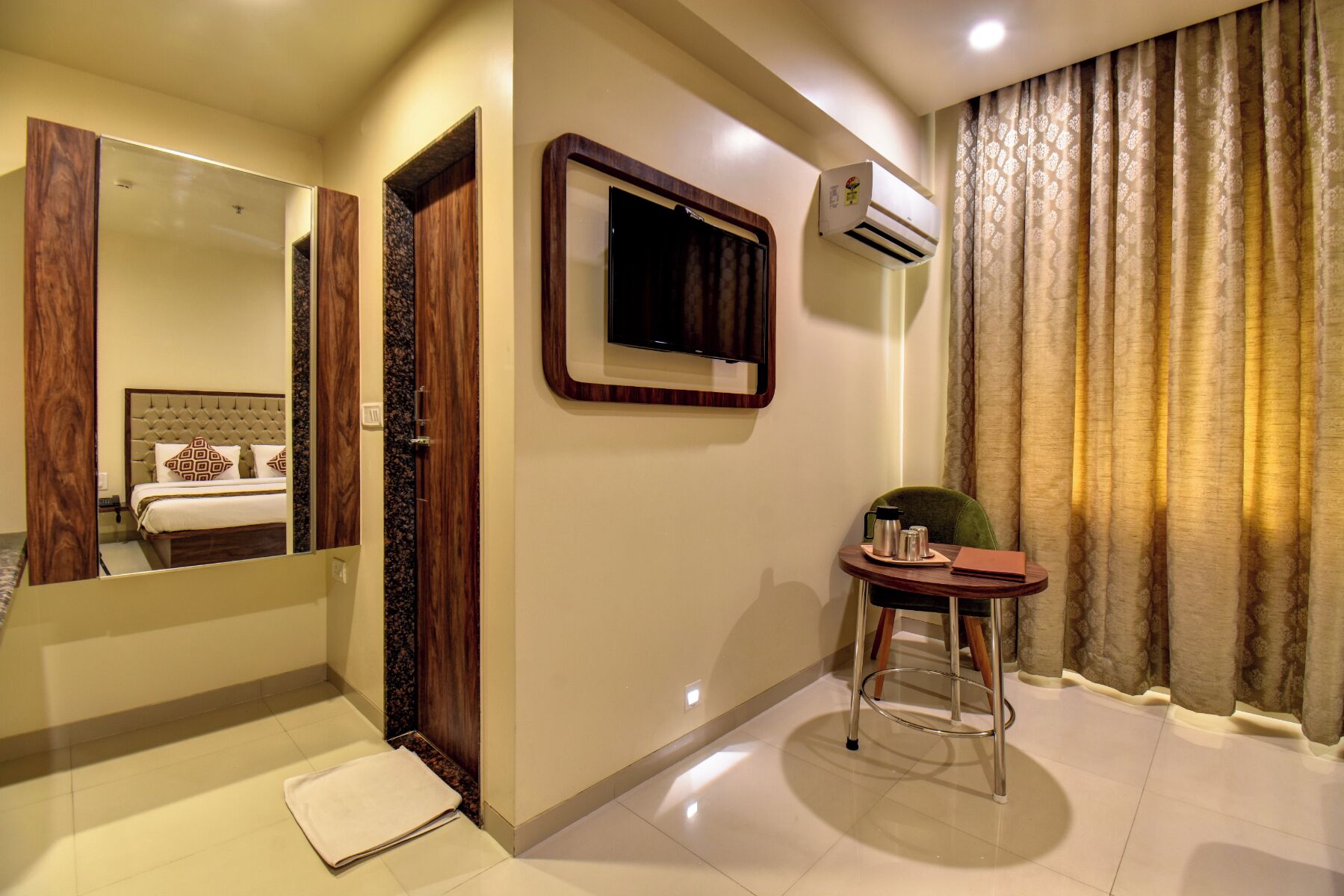 Une chambre d’hôtel comprenant un lit, un miroir, une petite table avec une chaise, un appareil de climatisation et une fenêtre avec des rideaux.