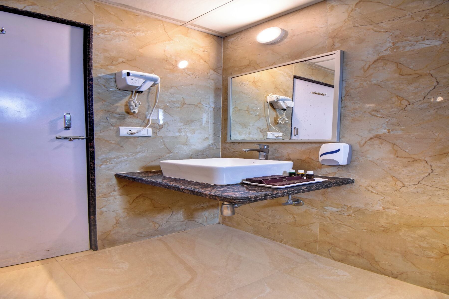 A bathroom with a marble wall, a white sink, a mirror, and a hairdryer mounted on the wall.