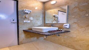A bathroom with a marble wall, a white sink, a mirror, and a hairdryer mounted on the wall.