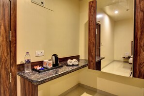 A hotel bathroom with a granite countertop, a mirror, a towel rack, and a bottle of water. - Bhagyalaxmi NX Hotel (Shirdi)