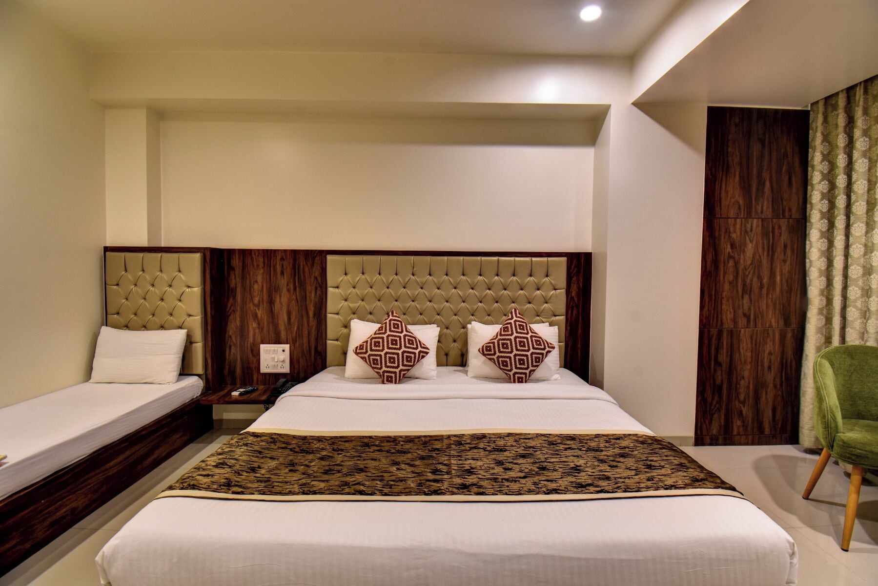 Habitación de hotel con una cama grande, dos mesitas de noche, una silla verde y un cabecero de madera.