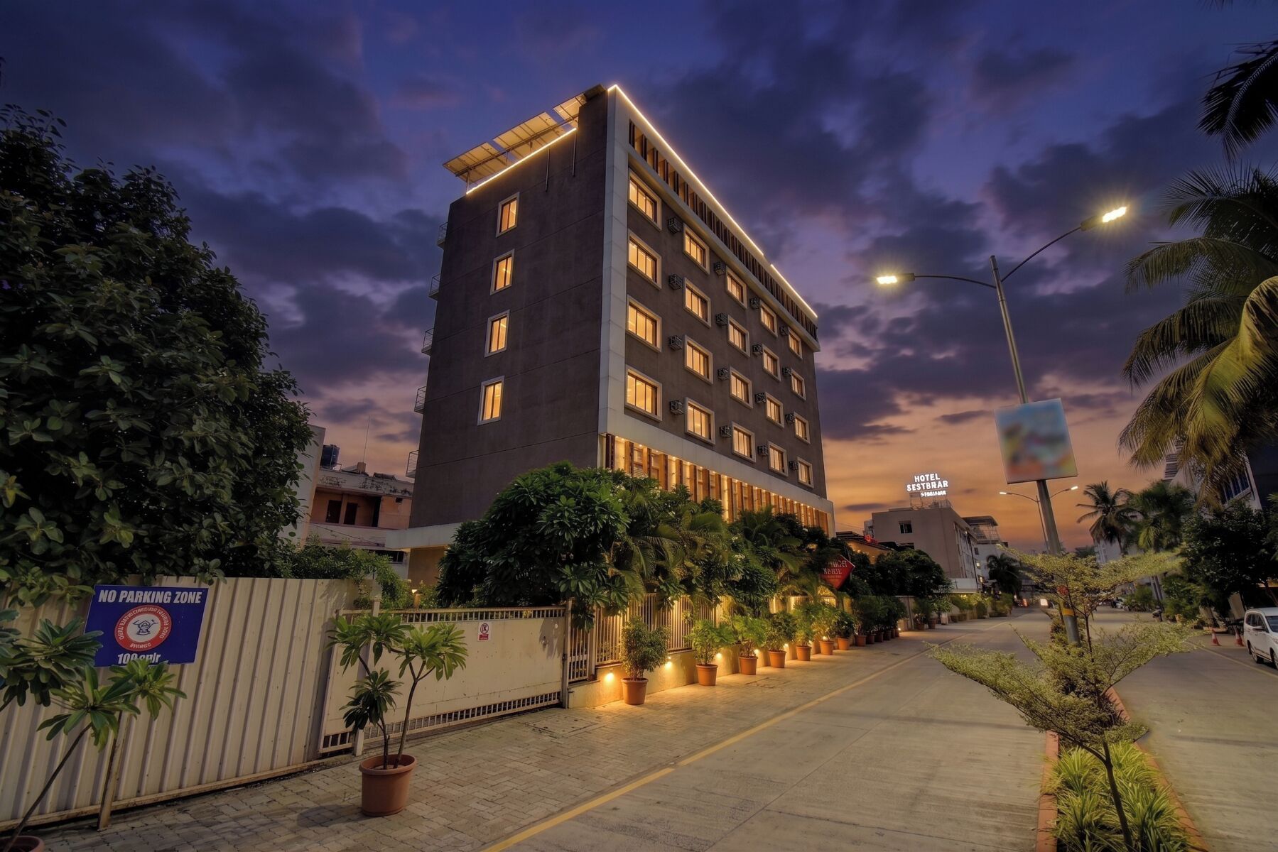 Un moderno edificio de hotel con varios pisos, una entrada protegida por una reja y un sendero bien iluminado que conduce a la entrada.