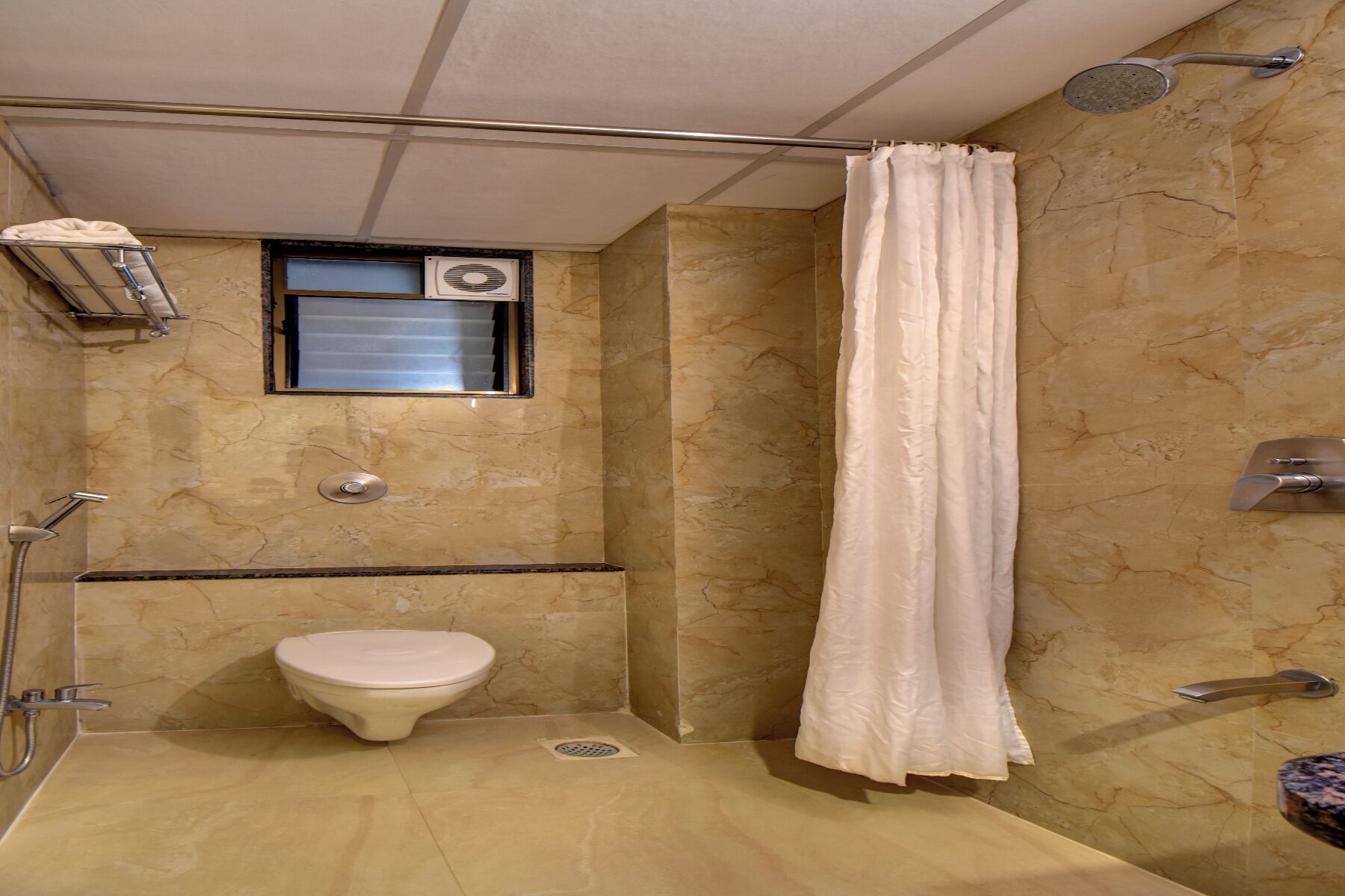 A bathroom with a shower, toilet, and a window with an air conditioning unit.