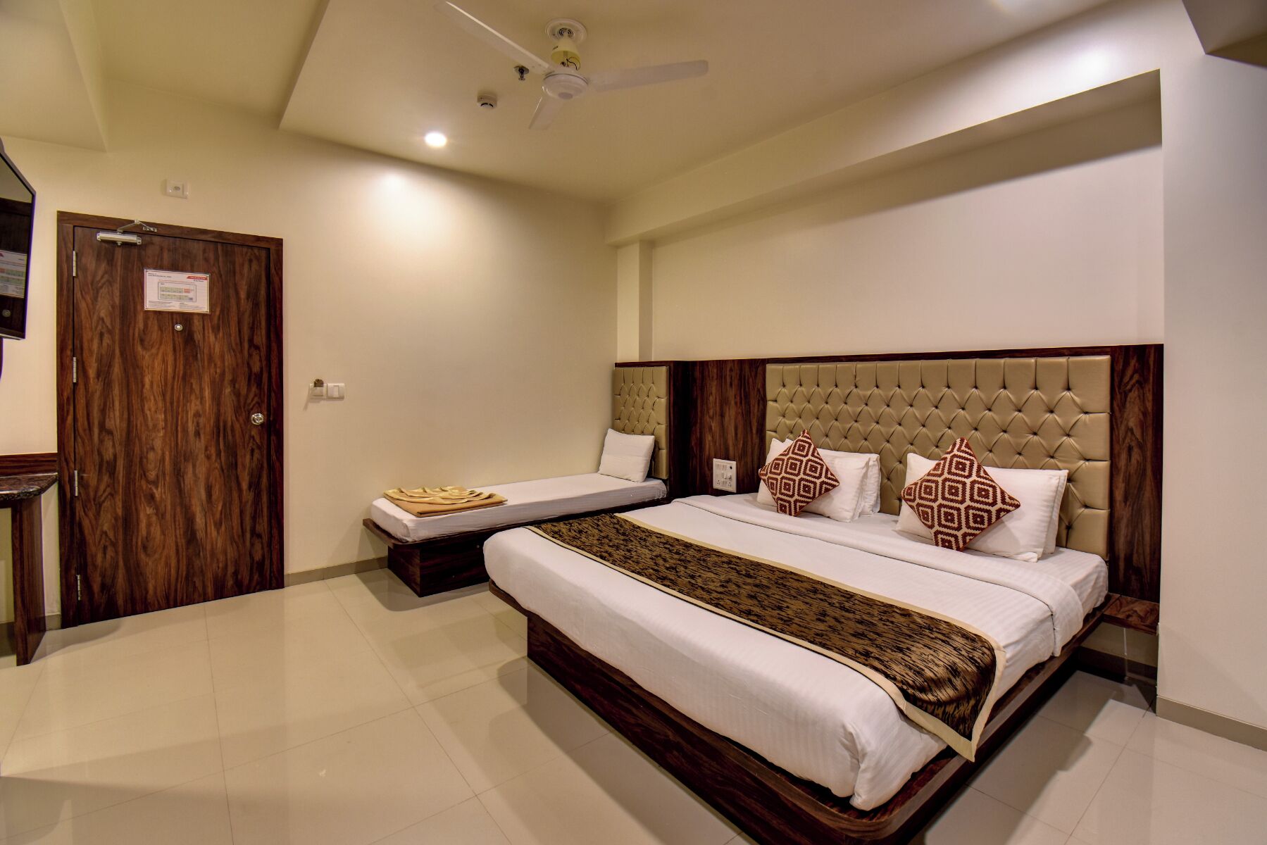 Habitación de hotel con dos camas, una puerta de madera y un ventilador de techo.