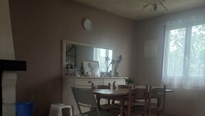 Uma área de refeições com mesa, cadeiras, transportador de animal de estimação, um balde azul e uma janela com luz natural.