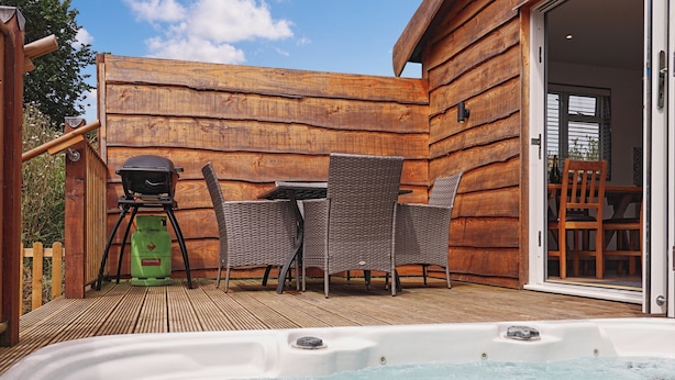 Un jacuzzi en primer plano, una mesa de patio con sillas y un tanque de propano al fondo.