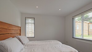 A bedroom with a wooden headboard, a double bed with white bedding, two windows with blinds, and a radiator. - 2 bedroom accommodation in Westward Ho! (Westward Ho!)