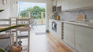 A modern kitchen with wooden cabinets, a built-in oven, and a dining area with a table and chairs. - 2 bedroom accommodation in Westward Ho! (Westward Ho!)