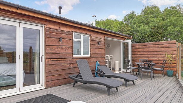 A wooden cabin with a deck, a hot tub, lounge chairs, and a dining area. - 2 bedroom accommodation in Westward Ho! (Westward Ho!)