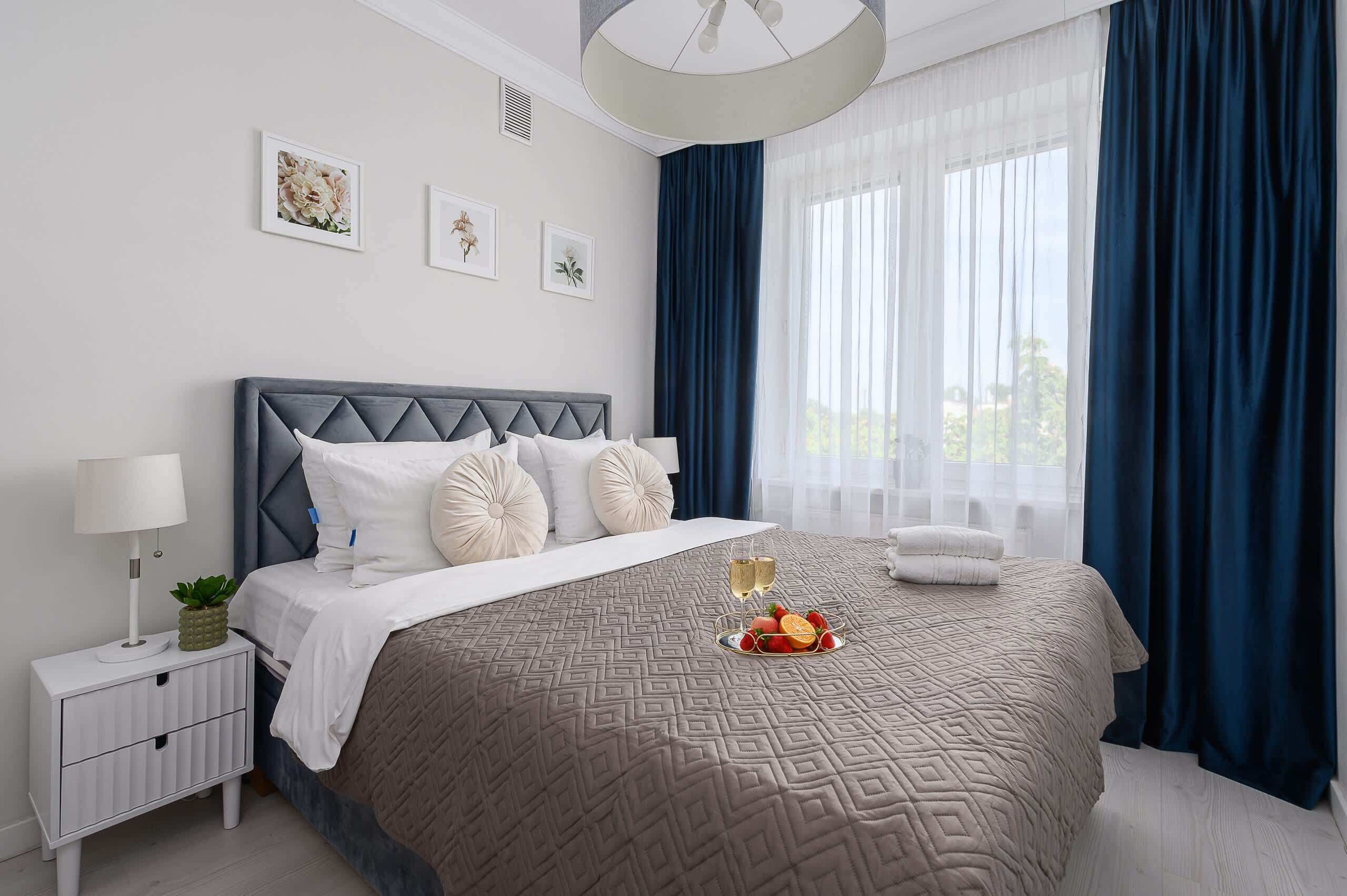 Une chambre d’hôtel moderne avec un grand lit, une table de chevet avec une lampe et une fenêtre avec des rideaux.