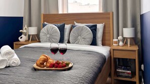 A neatly made bed with a quilted blanket, two bedside lamps, a tray with croissants and strawberries, and a window with curtains. - Lumina Comfort Apart near ZOO Orientarium with Parking (Łódź)