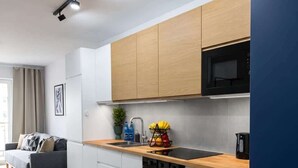 A modern kitchen with white cabinets, a black microwave, and a wooden countertop. - Lumina Comfort Apart near ZOO Orientarium with Parking (Łódź)