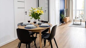 A modern dining area with a round table, black chairs, and a vase of yellow flowers. - Lumina Comfort Apart near ZOO Orientarium with Parking (Łódź)