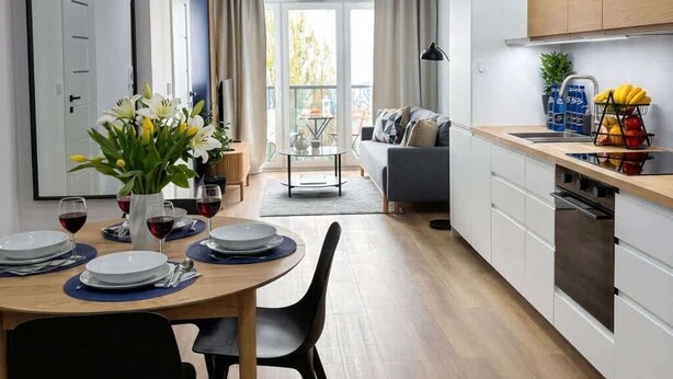 A modern kitchen with a dining area, a sofa, and a view of the outdoors. - Lumina Comfort Apart near ZOO Orientarium with Parking (Łódź)