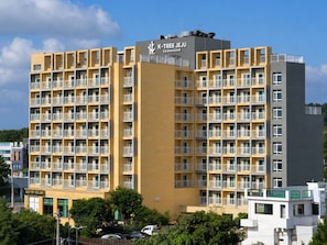 Un hôtel à plusieurs étages, doté d’une façade jaune, de balcons à chaque étage et d’un bar avec piscine sur le toit.