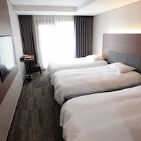 Habitación de hotel con dos camas, un escritorio, una silla y un ventanal con cortinas.