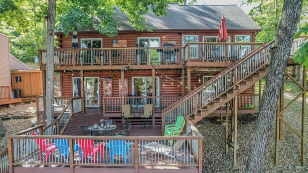 Eine zweistöckige Holzhütte mit Balkon, Sitzgelegenheit im Freien und einer Treppe.