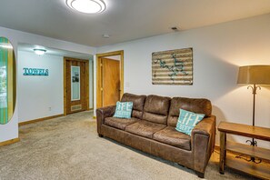 Ein Wohnzimmer mit braunem Ledersofa, zwei passenden Kissen, einem Holztisch, einer Lampe und einer an der Wand hängenden Karte.