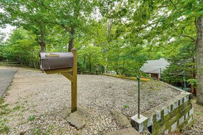 Une boîte aux lettres fixée à un poteau en bois, dans un espace recouvert de gravier, avec des arbres en arri ère-plan.