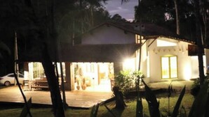 A house with a porch, a car parked outside, and a well-lit interior.