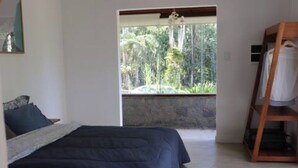 A bedroom with a bed, a wooden shelf, and a window with a view of greenery.