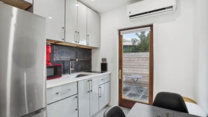 A modern kitchen with stainless steel appliances, white cabinetry, and a dining area with a table and chairs. - Marina Row 3 Beach, Shops (Delray Beach)