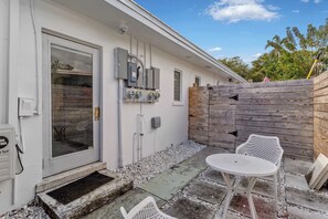 Eine Terrasse mit weißem Tisch und Stühlen, einem Holzzaun und Außenverteilerkästen.