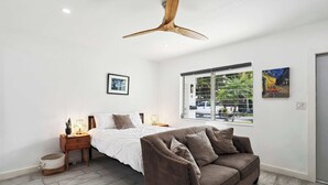 A modern bedroom with a bed, a brown sofa, a wooden nightstand, a floor lamp, and a ceiling fan. - Marina Row 3 Beach, Shops (Delray Beach)