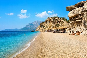 Une plage de galets avec une eau claire, une falaise rocheuse et des parasols.