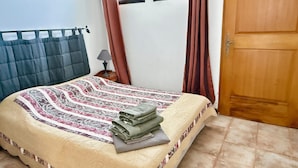 A neatly made bed with a patterned bedspread, a bedside lamp, and a window with curtains. - Two-bedroom apartment on the beach, right on the water, near shops (Olmeto)