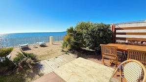 A patio with a view of the sea, wooden furniture, and a tiled floor. - Two-bedroom apartment on the beach, right on the water, near shops (Olmeto)