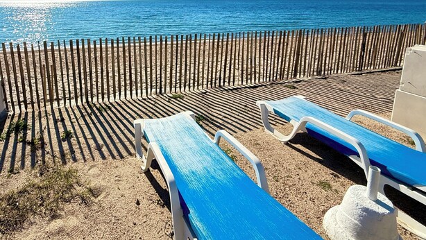A beach with a wooden fence, two blue lounge chairs, and a clear view of the sea. - Two-bedroom apartment on the beach, right on the water, near shops (Olmeto)