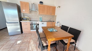 A compact kitchen with a refrigerator, microwave, oven, and dishwasher. There is a wooden dining table with chairs and a small island with a kettle. - Two-bedroom apartment on the beach, right on the water, near shops (Olmeto)
