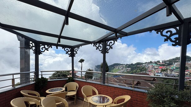 Un balcon avec des fauteuils en osier et une table, donnant sur une ville située sur une colline.