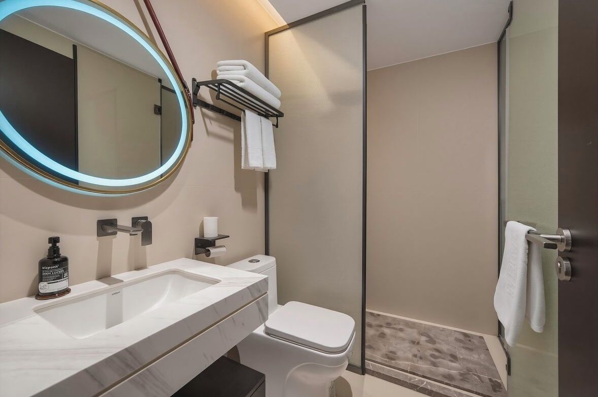 Un baño moderno con un espejo grande, un inodoro, un lavamanos y una cabina de ducha con mampara de vidrio.