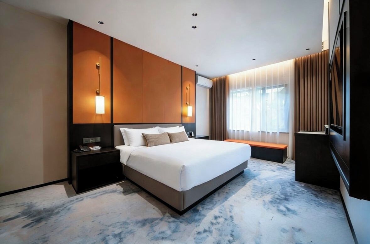 Una habitación de hotel moderna con una cama grande, mesitas de noche, un banco, un televisor y una ventana con cortinas.