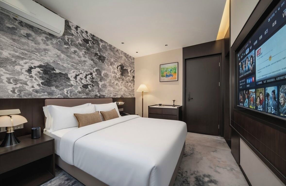 A hotel room with a bed, a nightstand, a TV, and a wall with a textured design.