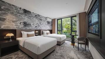 A modern hotel room with two beds, a large window with a view, a small table, and a wall-mounted TV.
