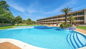 Um hotel com piscina, um edifício de vários andares e área ajardinada com árvores.