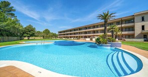Ein Hotel mit Schwimmbad, einem mehrstöckigen Gebäude und einer begrünten Anlage mit Bäumen.