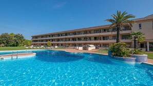 Um hotel com piscina, várias varandas e um jardim bem cuidado.