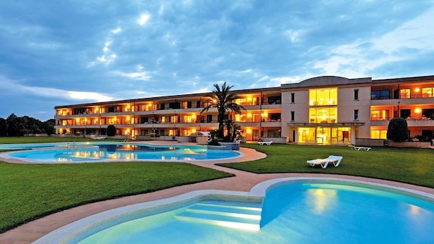 Um hotel com várias varandas, uma piscina e um gramado bem cuidado.
