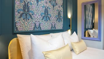 Een bed met witte en gouden kussens, een groot kunstwerk met bloemenprint en een spiegel met paars frame.