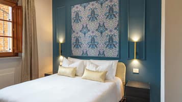 A bedroom with a bed, two bedside lamps, a window with curtains, and a wall with a floral pattern.