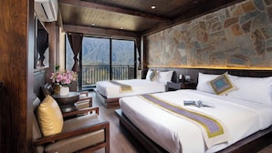 Quarto de hotel com parede de pedra, duas camas, teto de madeira, varanda e vista para montanhas.